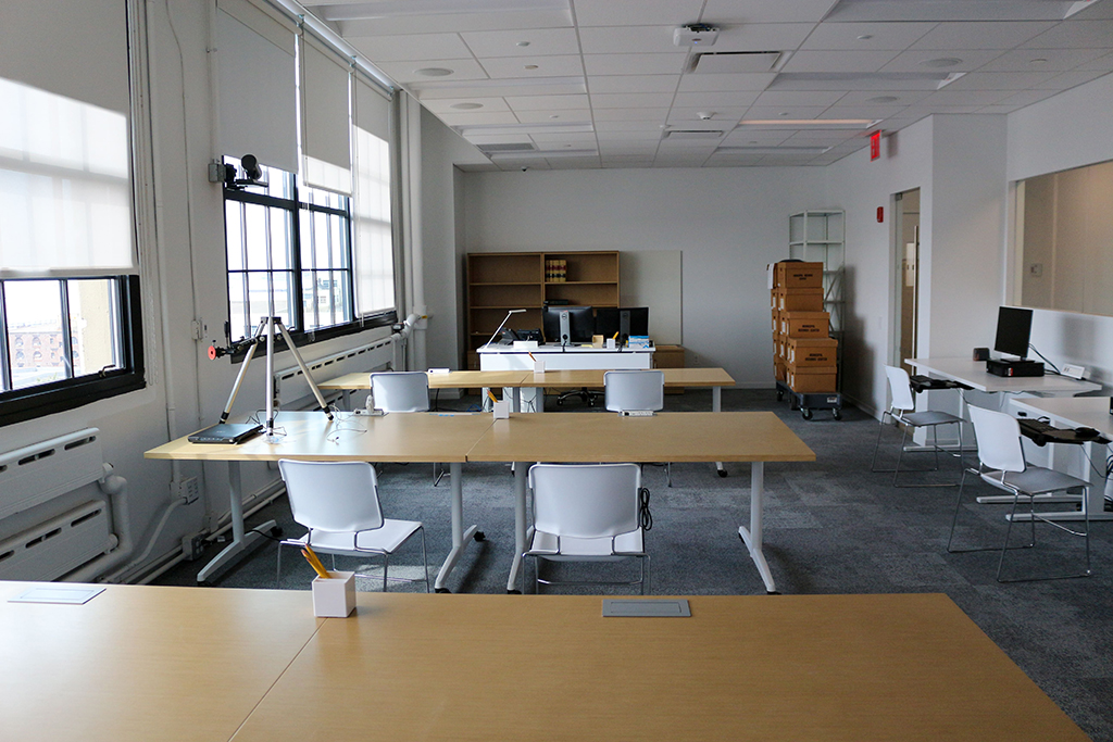 Color image of the new research room showing five wood desks, white chairs, a computer and bookcase.